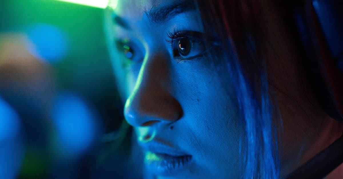 Intense close-up of a focused gamer wearing headphones illuminated by vibrant neon lighting.