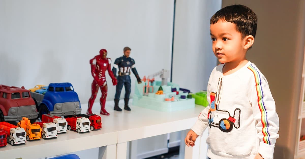 Young boy playing with toy cars and action figures at home.