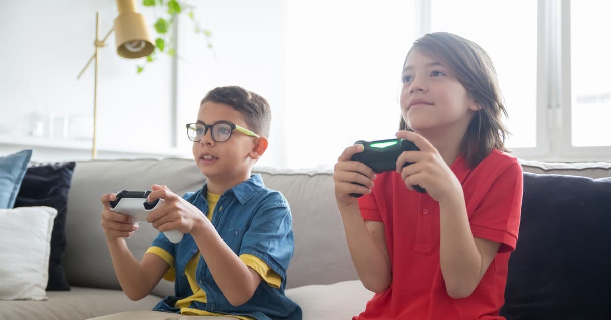 Two kids playing video games on a cozy couch indoors, showcasing fun and technology.
