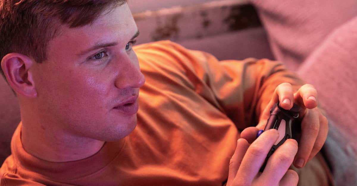 A young man plays video games on a comfortable couch, fully immersed in the experience.