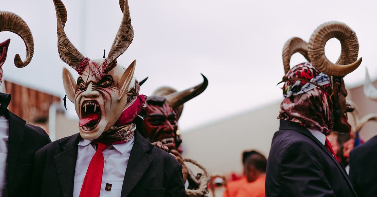 Men in elaborate devil masks perform a traditional folk dance outdoors.