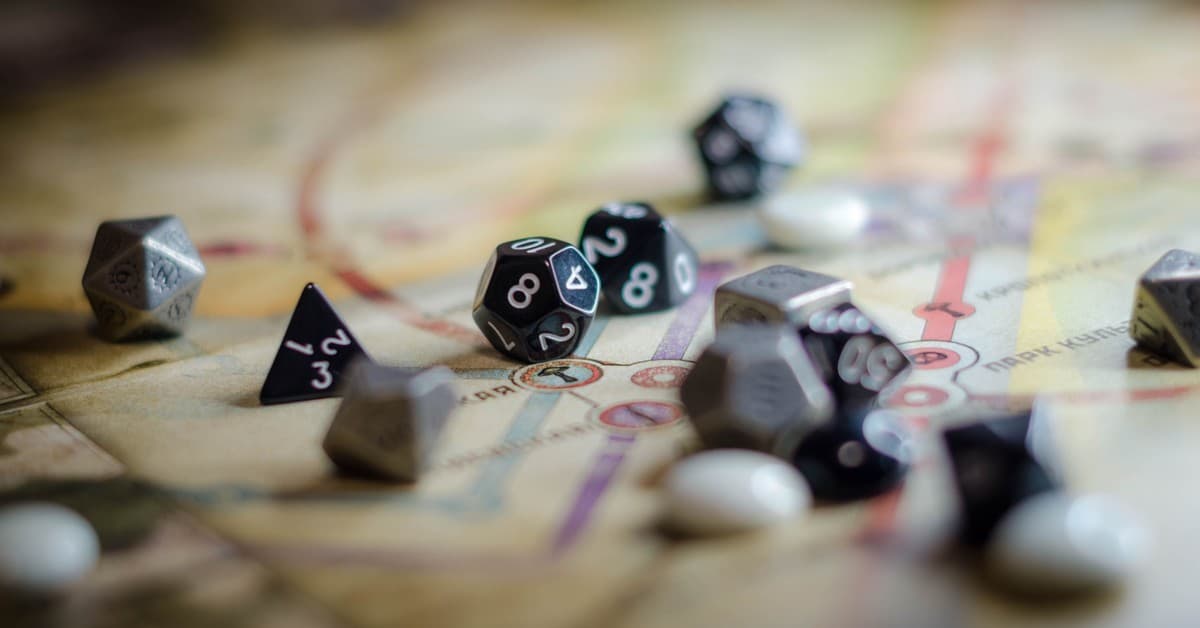 Focus on black and white polyhedral dice scattered on a board game map, suggesting strategy and chance.