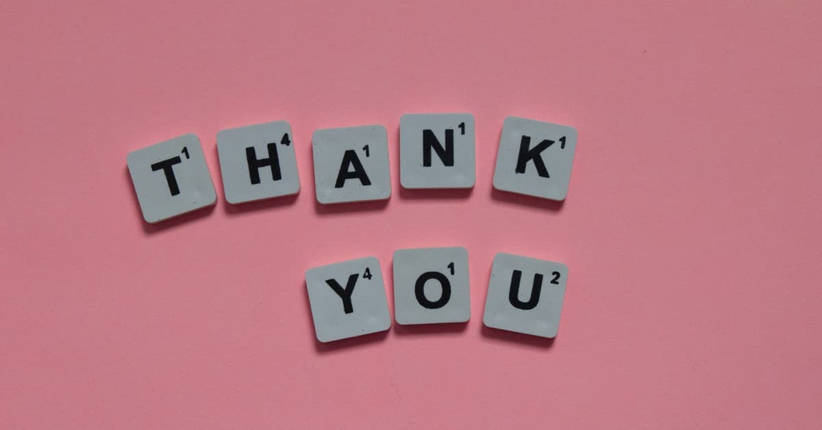 Scrabble tiles forming 'Thank You' on a pink background, ideal for gratitude concepts.