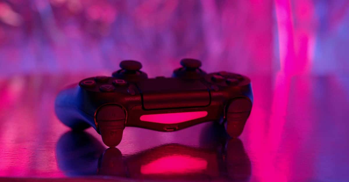 A wireless game controller in focus with a vibrant pink and purple neon background.