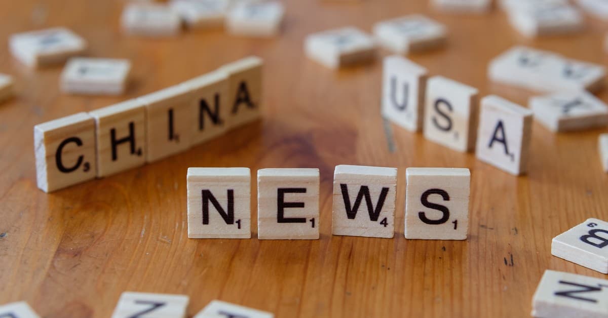 Wooden Scrabble tiles spelling 'NEWS' with 'CHINA' and 'USA' on a wooden surface.