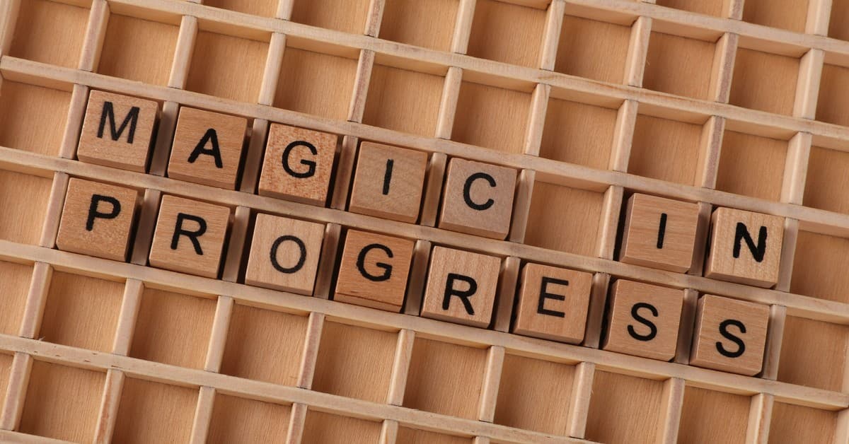 Wooden letter blocks arranged to spell 'Magic in Progress' on a grid.