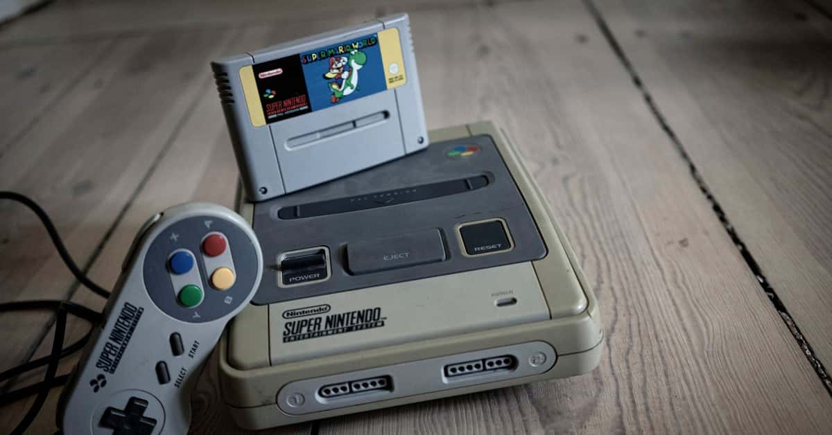 From above of aged video game console with cassette and controller with colorful buttons on wooden surface