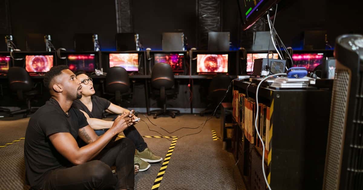 Two diverse men focused on gaming in a modern arcade setting, showcasing technology and camaraderie.