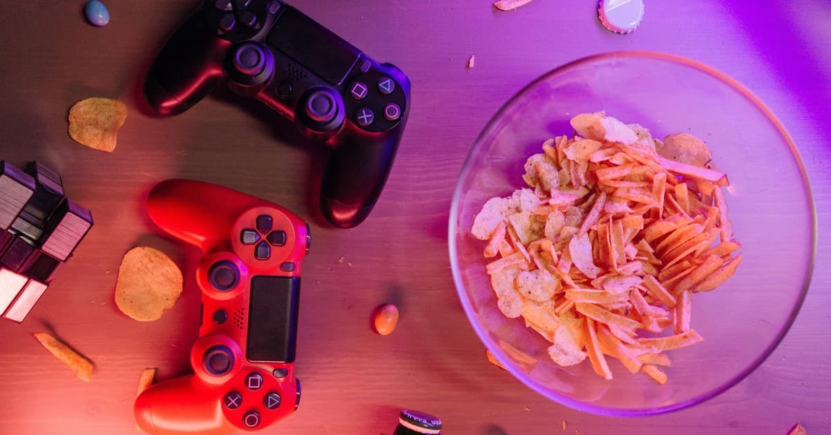 Overhead view of game controllers and snacks on a table, perfect for a gaming night setup.