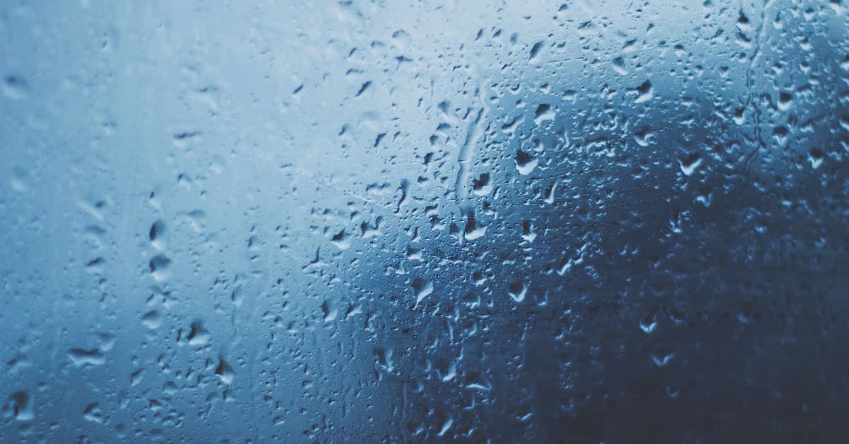 Detailed view of water droplets on a glass window with a blue background.