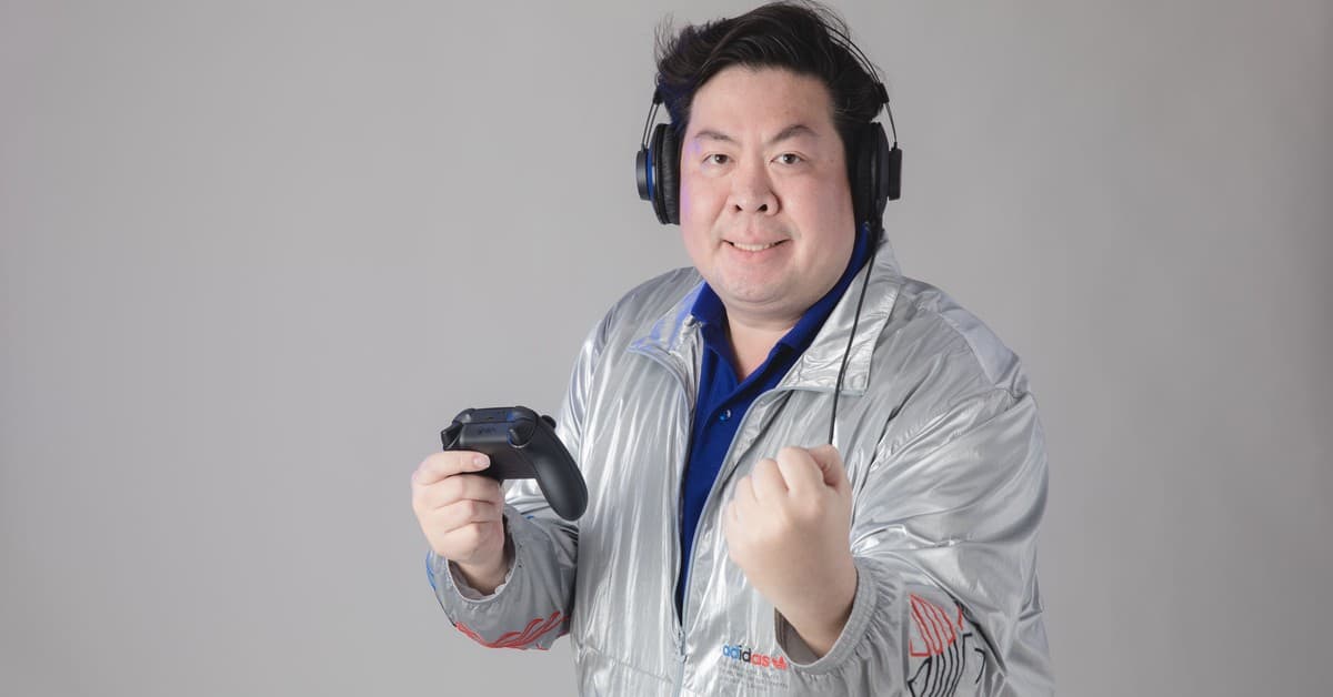 Asian man with headphones celebrates while gaming, holding a controller.