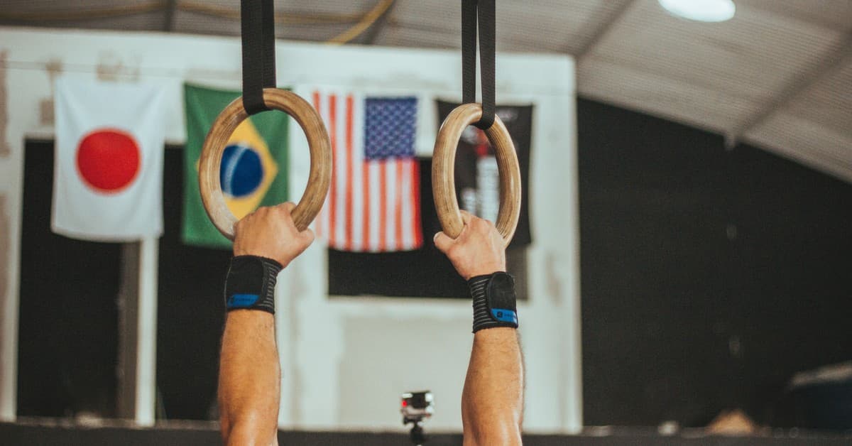 A gymnast performs on rings indoors, showcasing strength and skill.