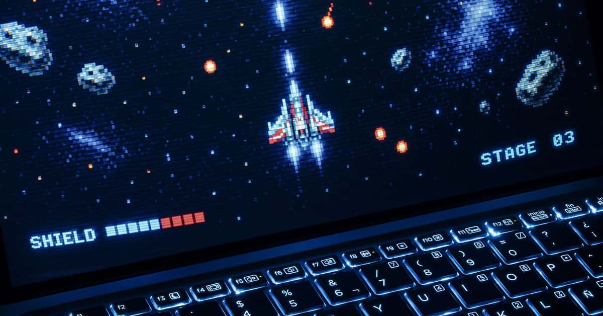 A classic arcade space shooter game displayed on a laptop with illuminated keyboard, showing retro graphics.