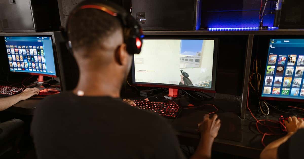 A man deeply engaged in a video game at a modern esports setup with multiple screens.
